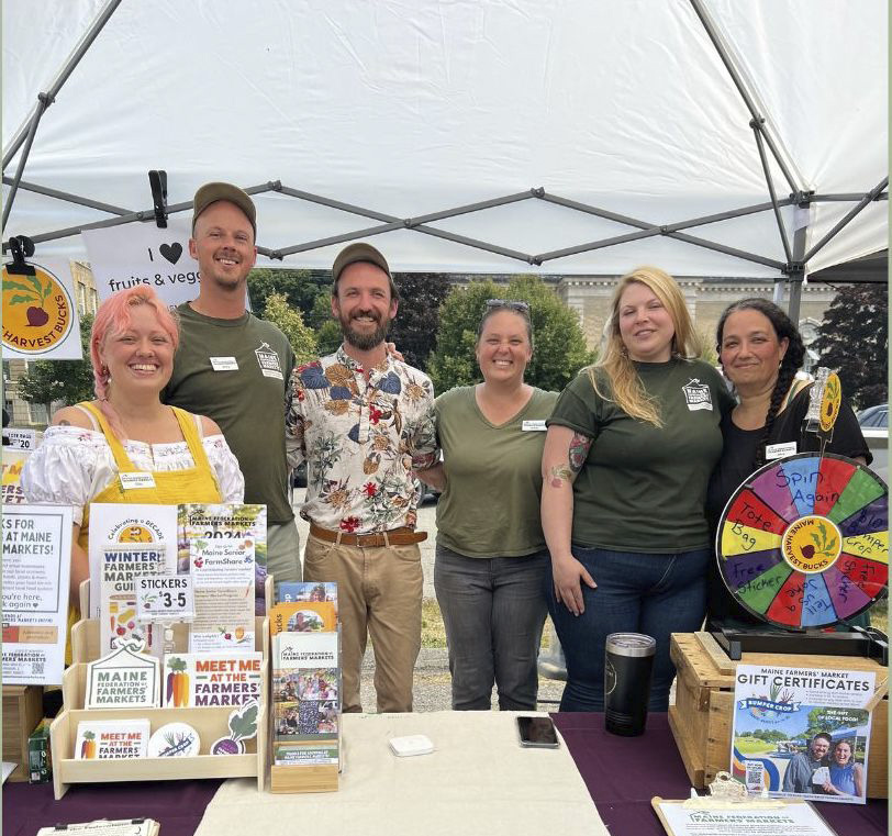 People standing behind a farmers market table